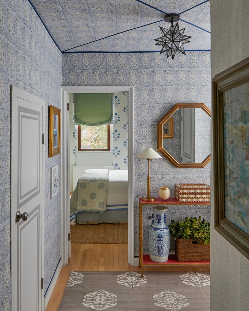 Corredor com papel de parede azul delicado na parede, espelho de madeira hexagonal e aparador de madeira