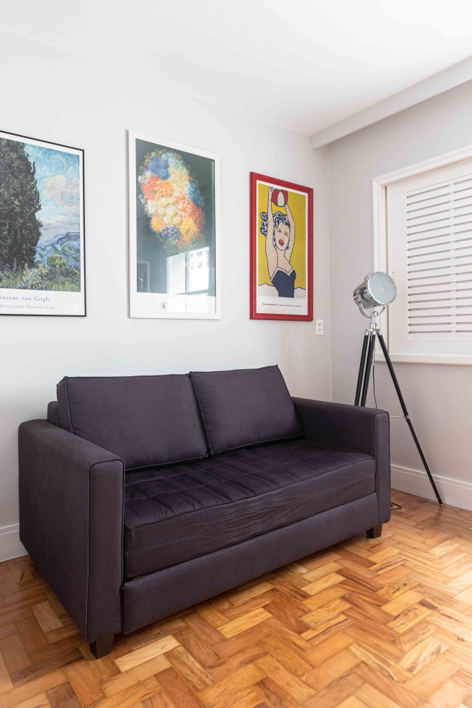 Home office com sofá preto e quadros coloridos na parede