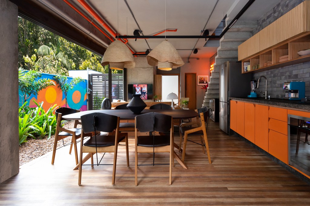 Sala integrada à área externa com mesa redonda, armários laranjas e estilo industrial