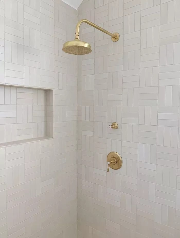 Banheiro com chuveiro dourado e paredes revestidas com azulejos brancos retangulares.