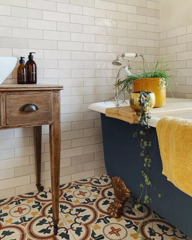 Este lindo banheiro da edwardian_seaside_home apresenta uma paleta de cores azul e amarela em todo o piso de cerâmica e na banheira com pés. Colocar uma cor em destaque é uma ótima maneira de manter o banheiro uniforme e com design intencional.