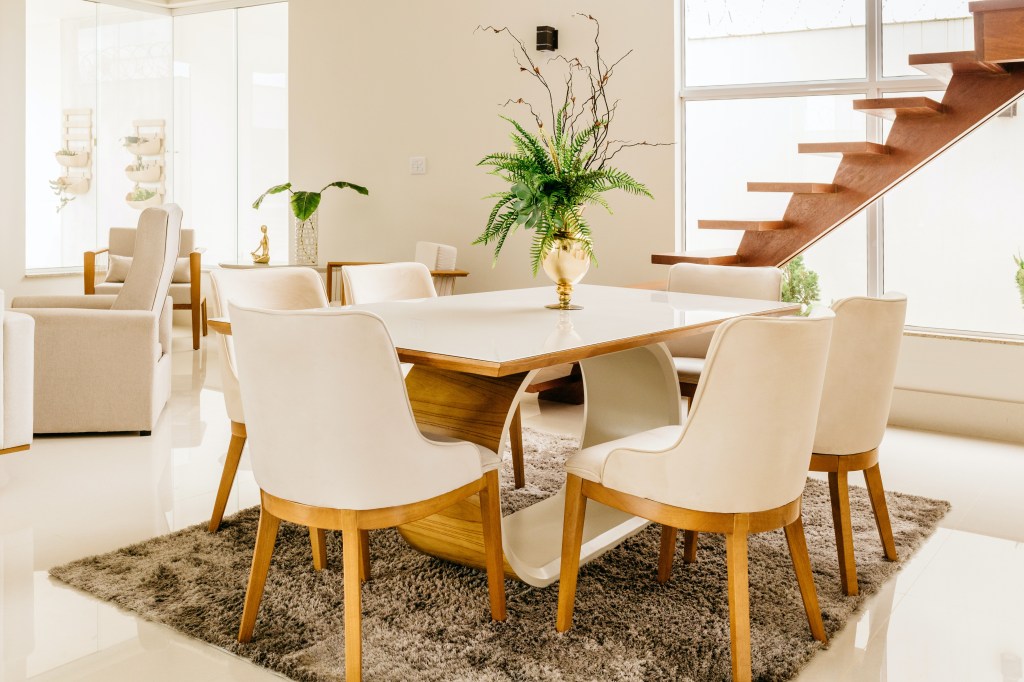 Sala de jantar com uma mesa de seis lugares, branca, com pés de madeira.