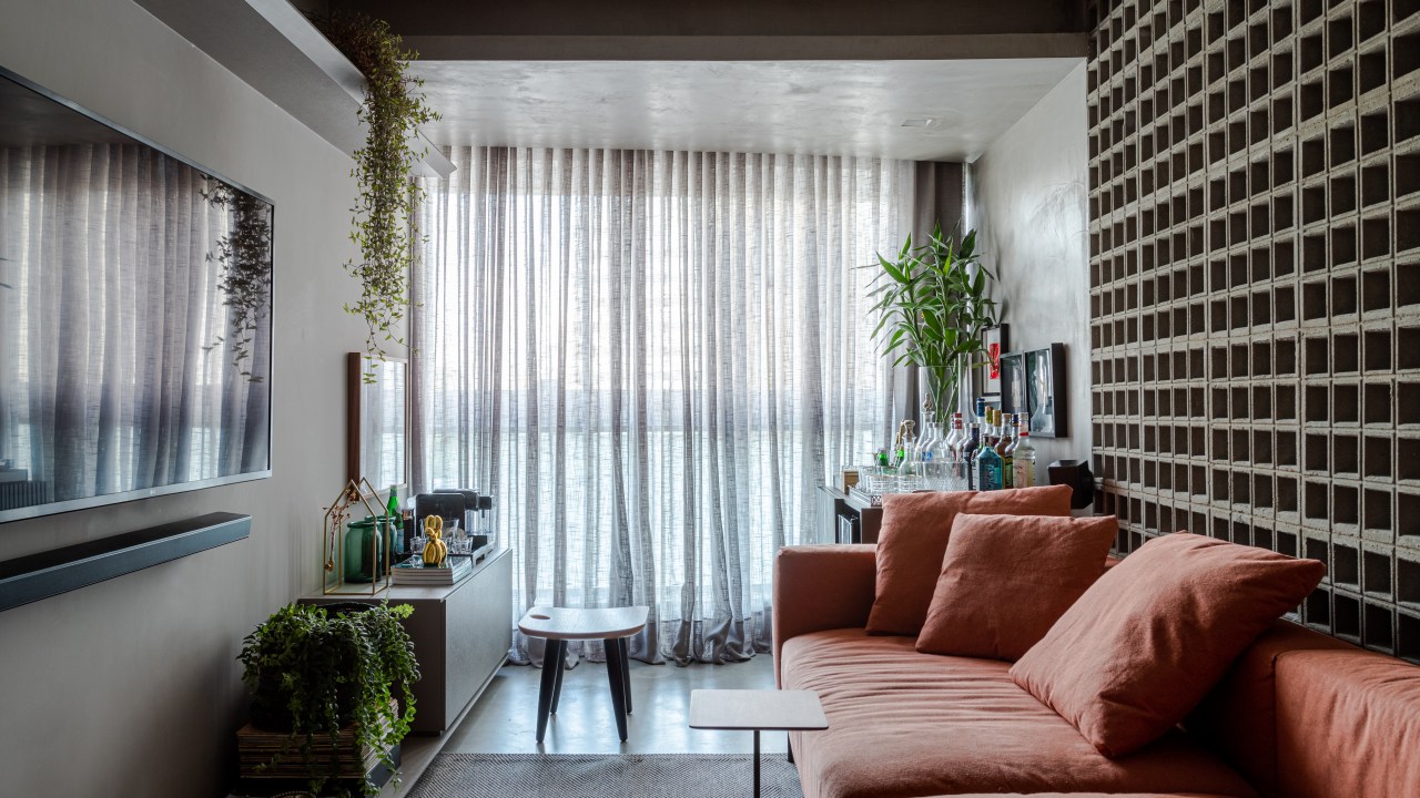sala com paleta cinza, sofá terracota e parede de cobogó