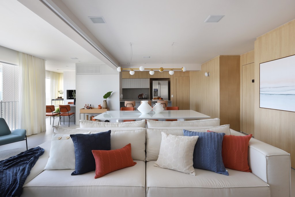 Sala de estar integrada com painel de madeira e sofá bege