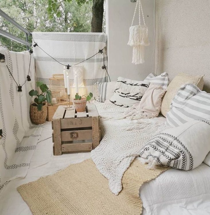 Varanda com sofá futon, decorada em tons de branco, bege e cinza, com muitas almofadas e cobertores.