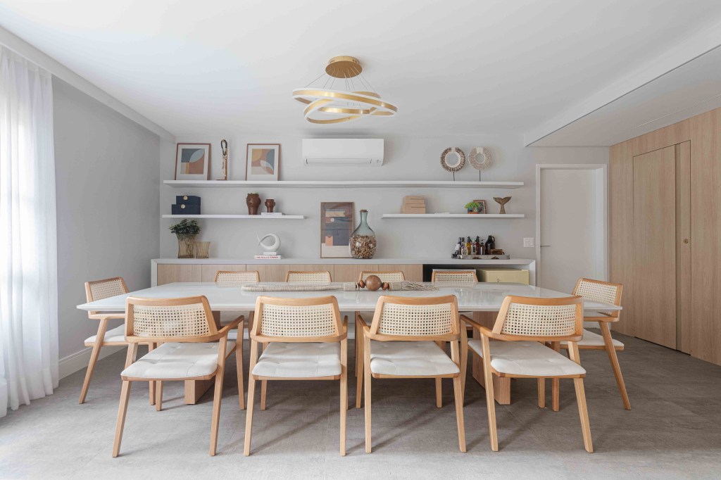 Sala de jantar com cadeiras de madeira e palhinha e parede com prateleiras