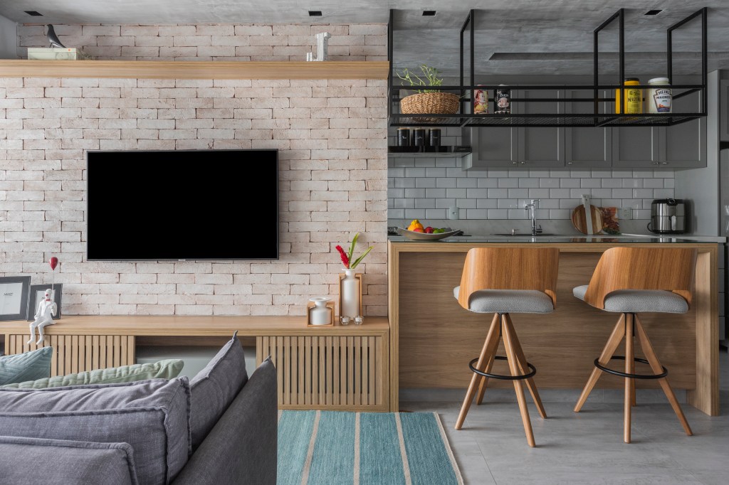 Sala de estar integrada com tijolinhos, madeira e sofá cinza