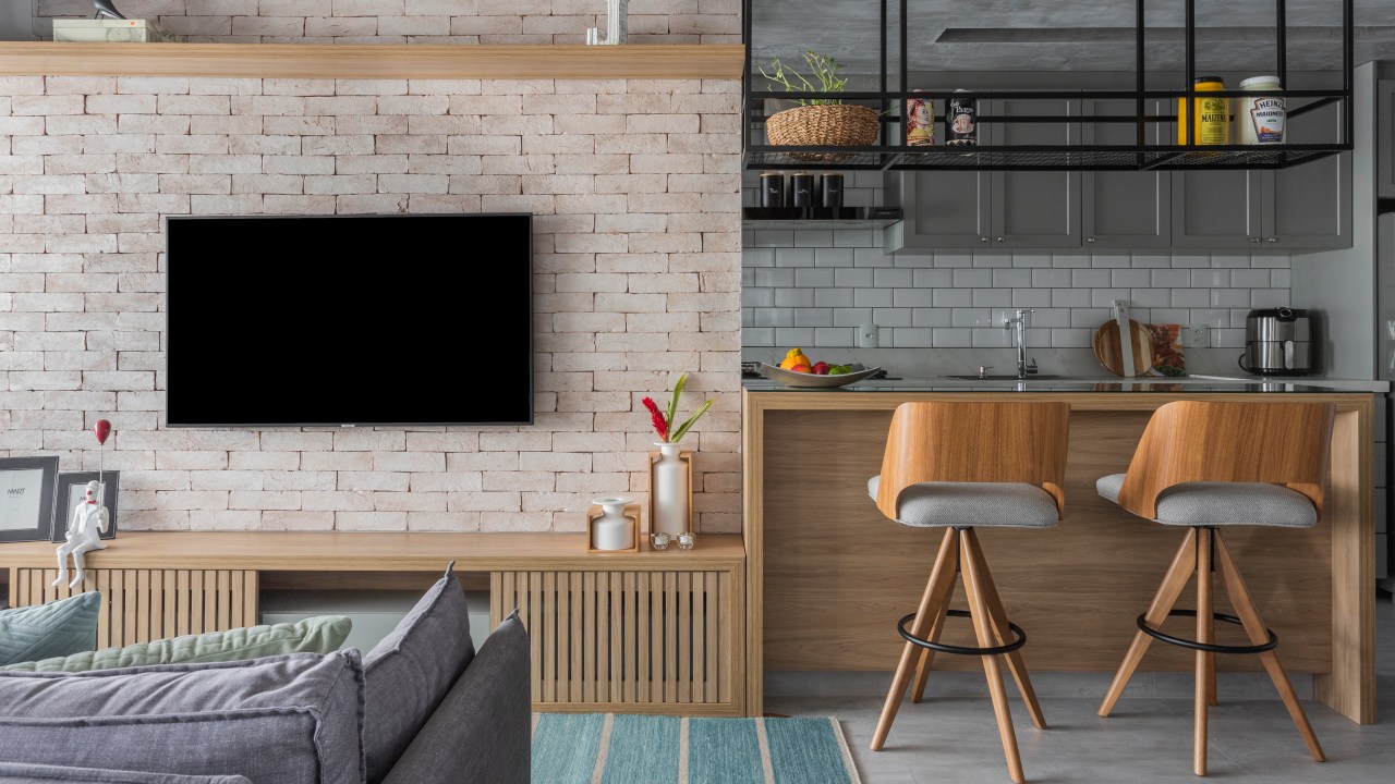 Sala de estar integrada com tijolinhos, madeira e sofá cinza