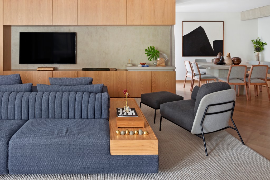 Sala de estar com sofá azul e poltrona cinza e painel de madeira para TV