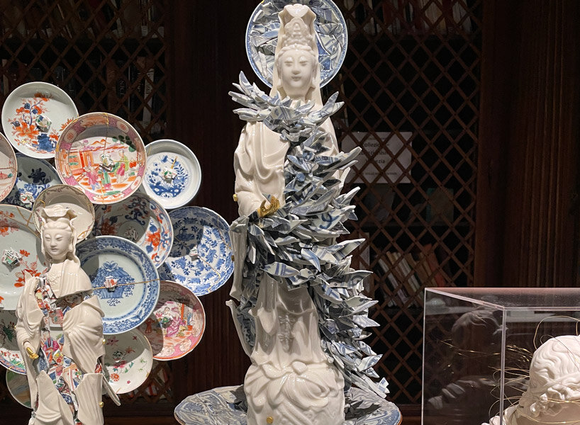 Escultura de cerâmica oca de corpo inteiro fragmentada. Os espaços onde ela está quebrada são preenchidos por cacos de cerâmica cuidadosamente empilhados.