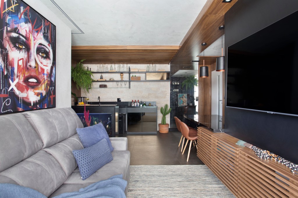 Sala de estar com sofá cinza; tv; home bar ao fundo