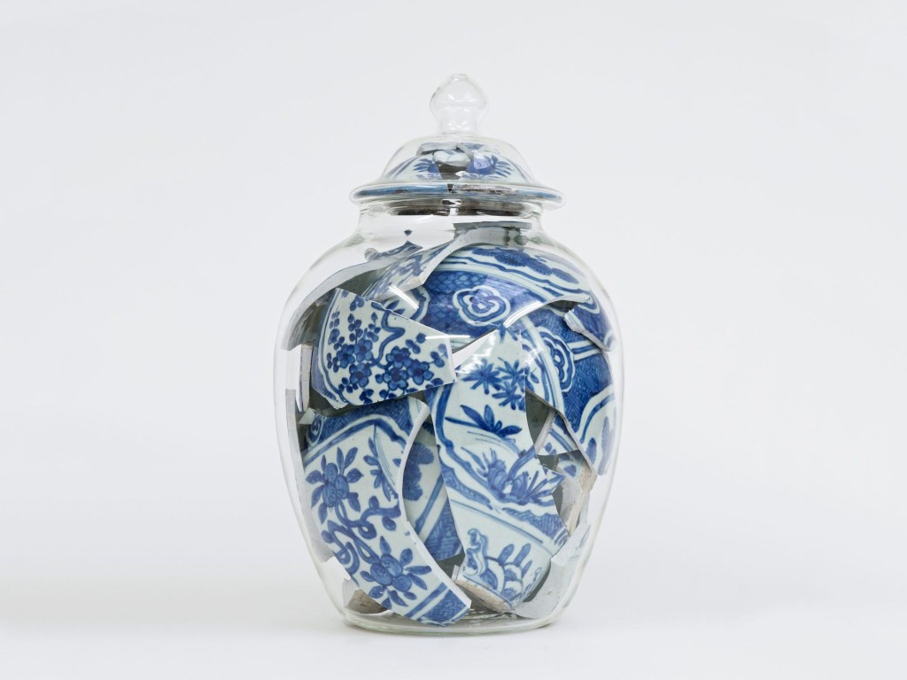 Vaso transparente preenchido por grandes cacos de um vasos de cerâmica estampado.