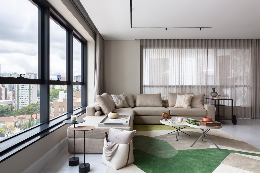 Sala com móveis e paredes em tons complementares de branco, bege e marrom. O destaque fica para o tapete verde.