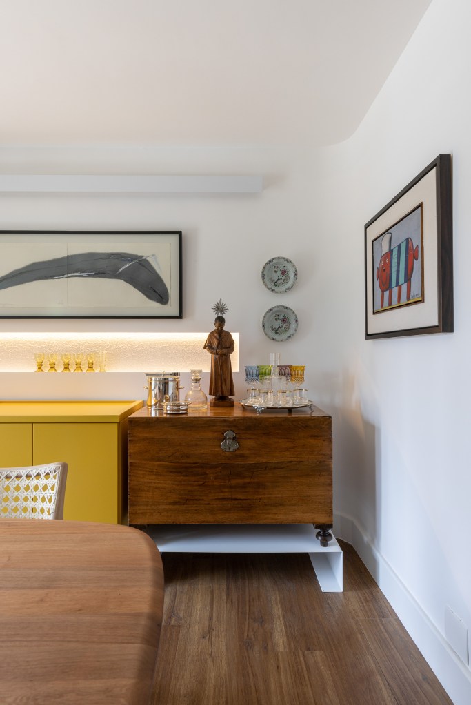 Sala de jantar com pendente; mesa em madeira com quatro lugares; aparador amarelo; nicho iluminado