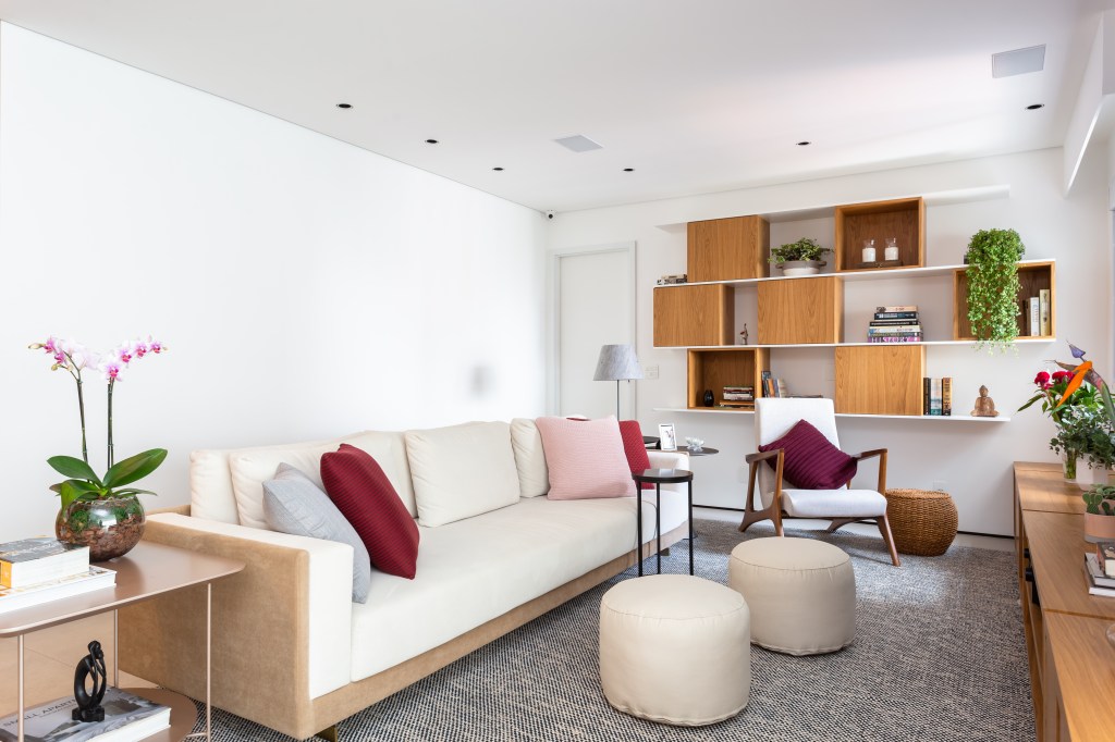 Sala de estar estreita com sofá branco de 3 lugares. A frente dois pufes pequenos, circulares, da mesma cor do sofá.