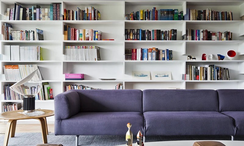 Sala com estante branca com livros e sofá roxo