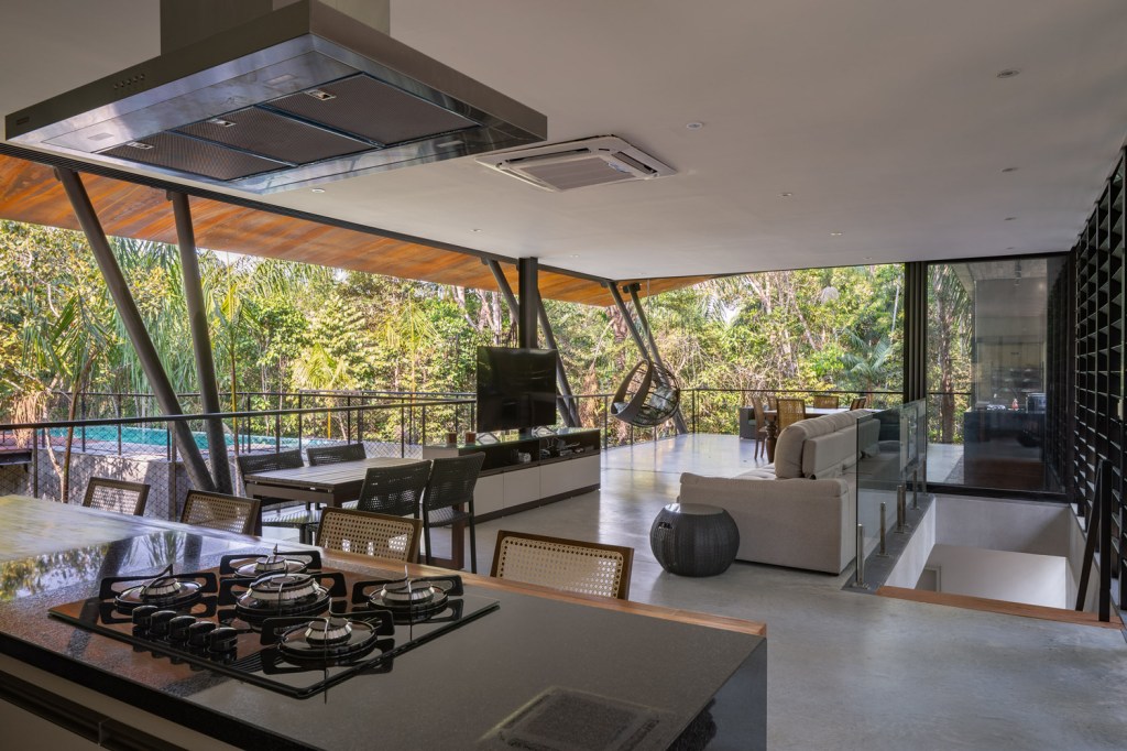Foto mostra parte da bancada da cozinha e da sala de jantar e estar, integradas à paisagem graças às grandes aberturas de vidro, de correr.