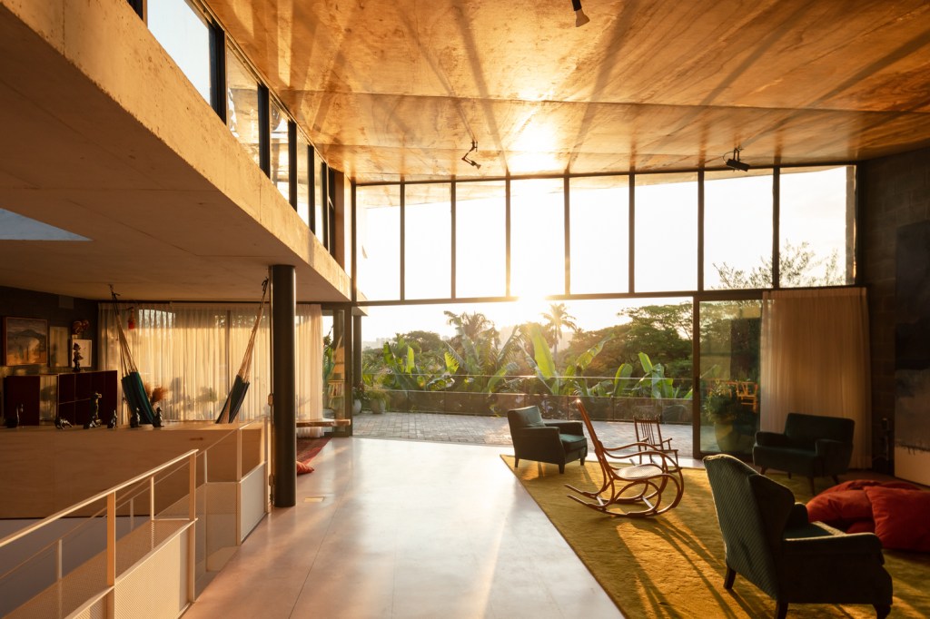 Sala de estar ampla com painéis de vidro recebe luz do sol ao entardecer.
