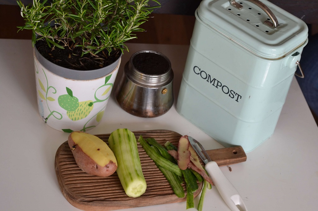 Mesa de cozinha com legumes descascados em tábua. Recipiente de compostagem ao lado