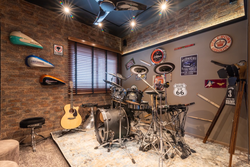 Sala de música com tapete, bateria, violão, paredes revestidas e visual de rock.