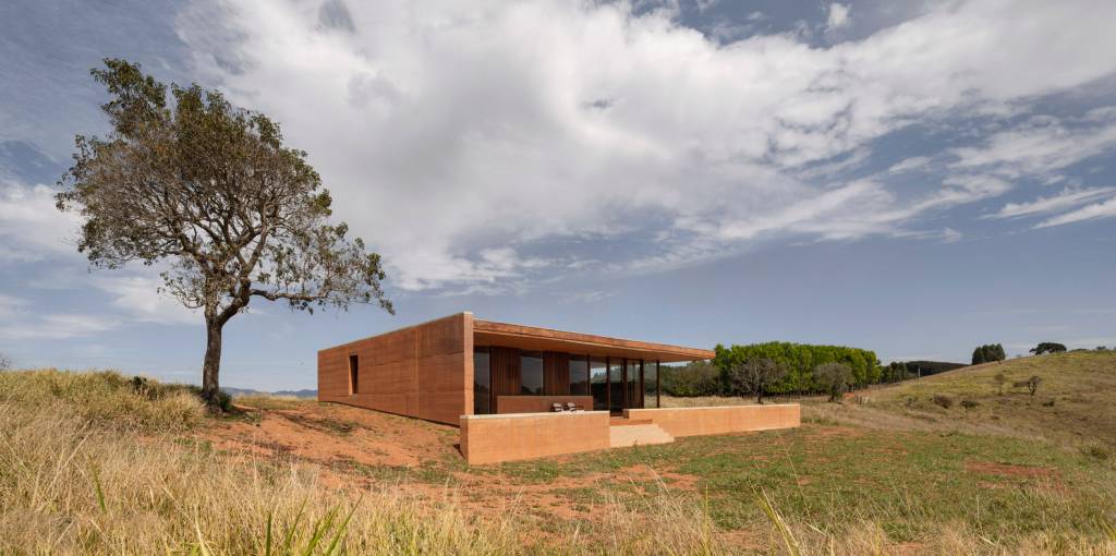 Fachada de casa em taipa de pilão, com linhas retas, em ambiente rural e isolada na paisagem.