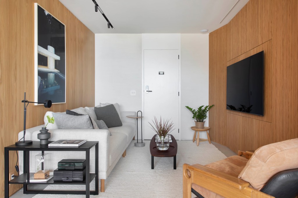 Sala de estar com painel de madeira para TV, sofá branco, tons neutros