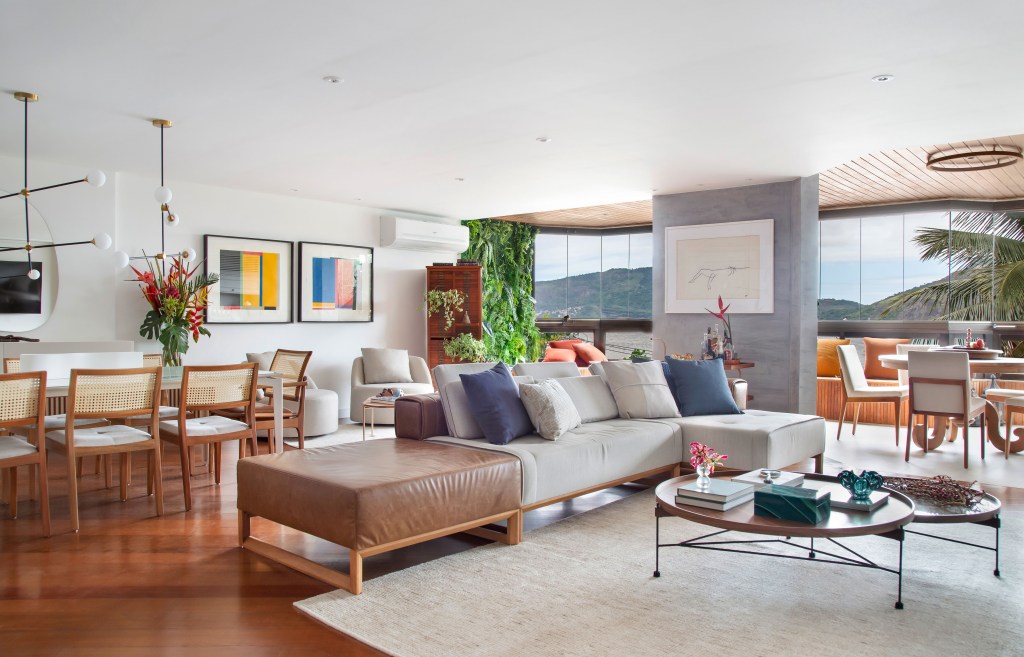 Sala de estar com sofá branco, piso de madeira, cadeira de madeira e palhinha e quadros coloridos