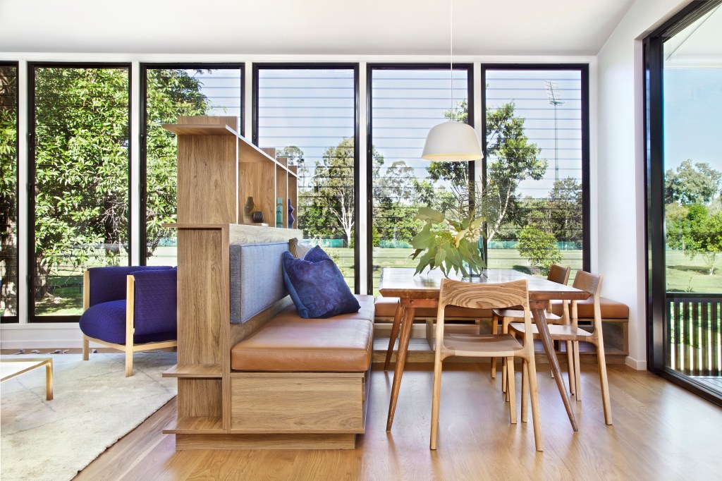 Sala com piso de madeira, sofá funcional cujo rodapé serve de estante e paredes de vidro
