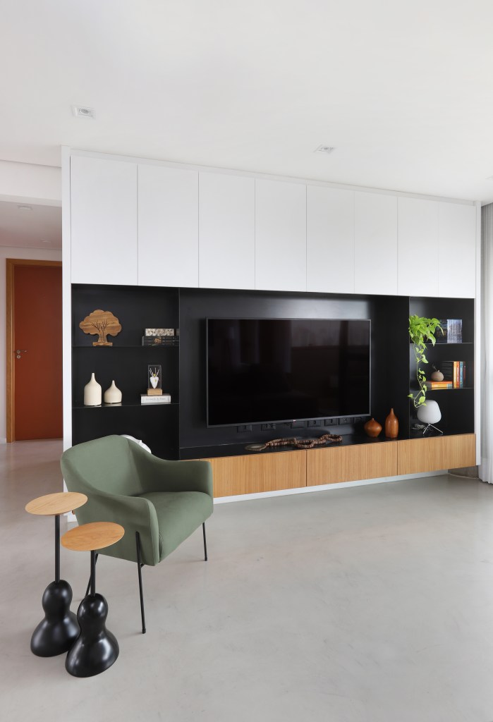 Painel preto para TV em sala de estar, poltrona verde e mesinha de madeira
