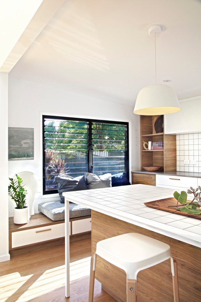 Cozinha com janela para exterior e natureza, bancada de pedra branca e luminária minimalista