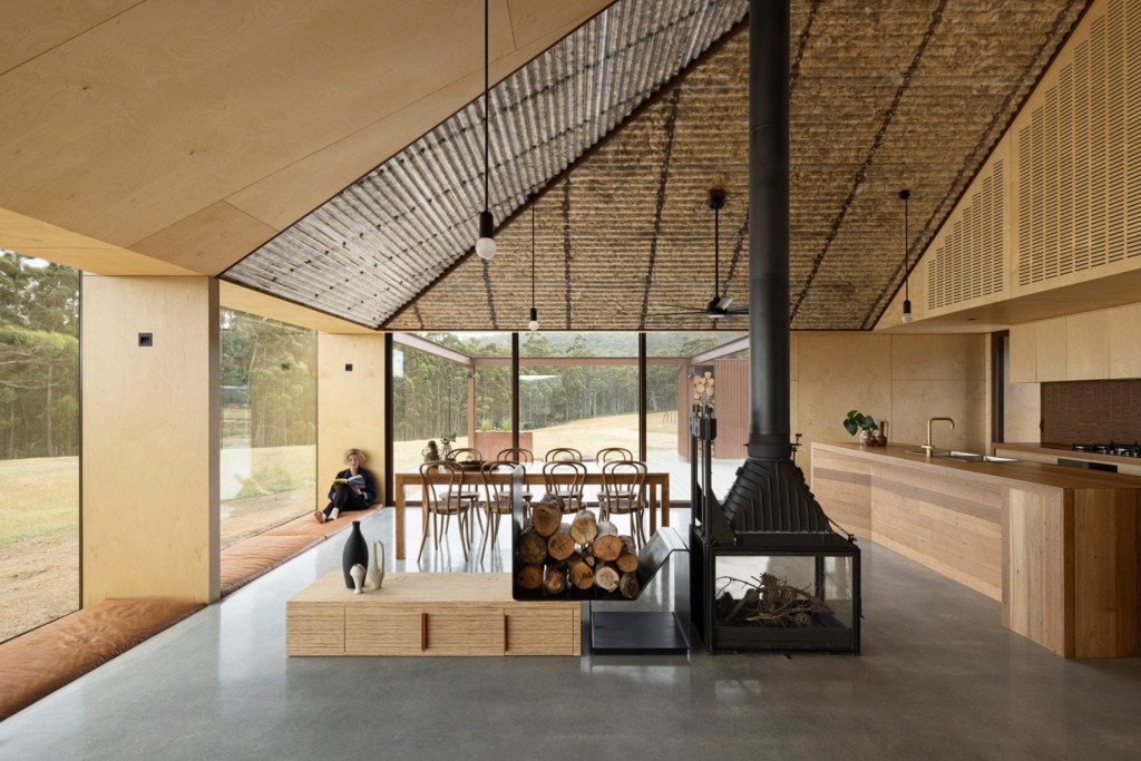 Cozinha ampla com portas de vidro para área externa. O ambiente é todo estruturado em madeira. O teto sem laje mostra o telhado forrado por lã.