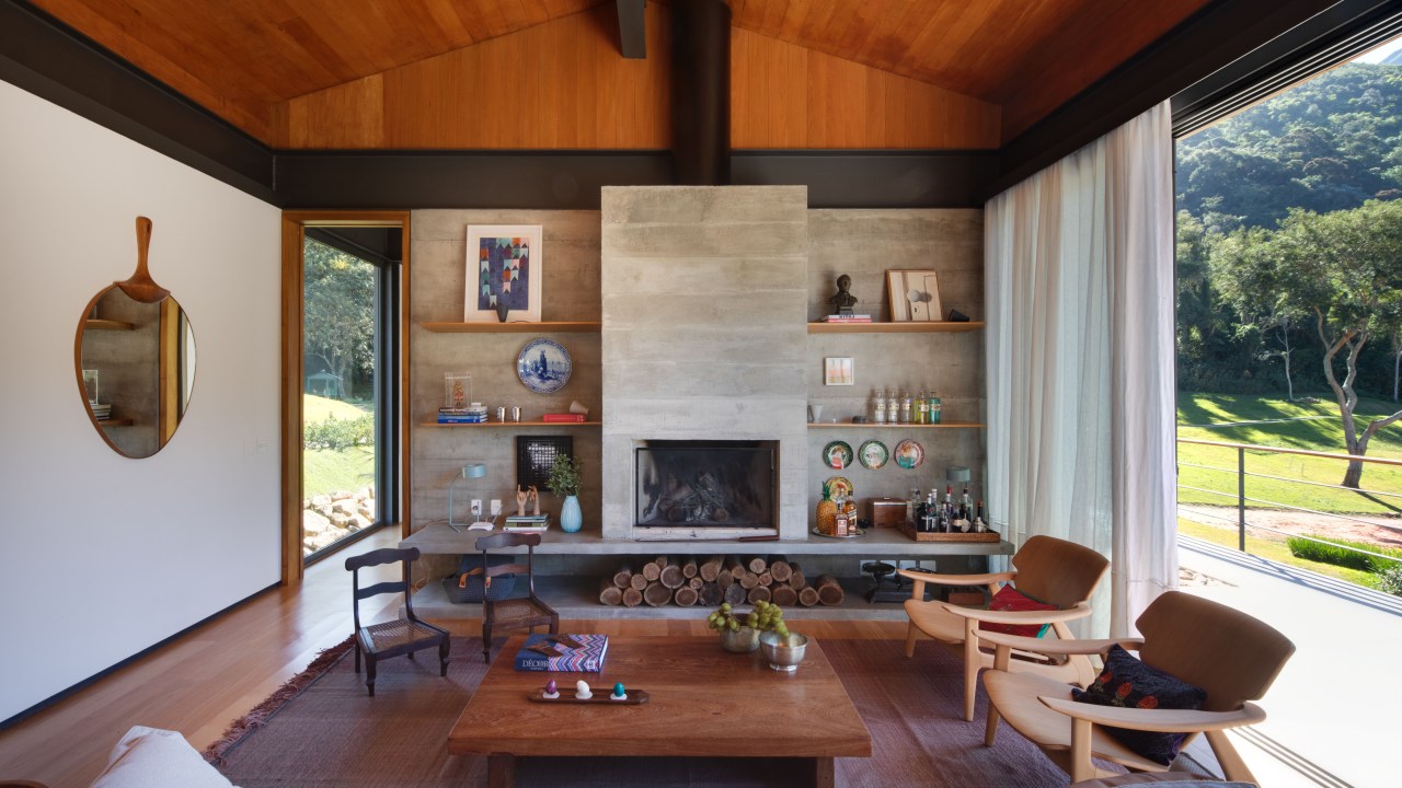 Sala de estar de casa de campo com teto de madeira, lareira, mesa de centro, sofá e poltronas