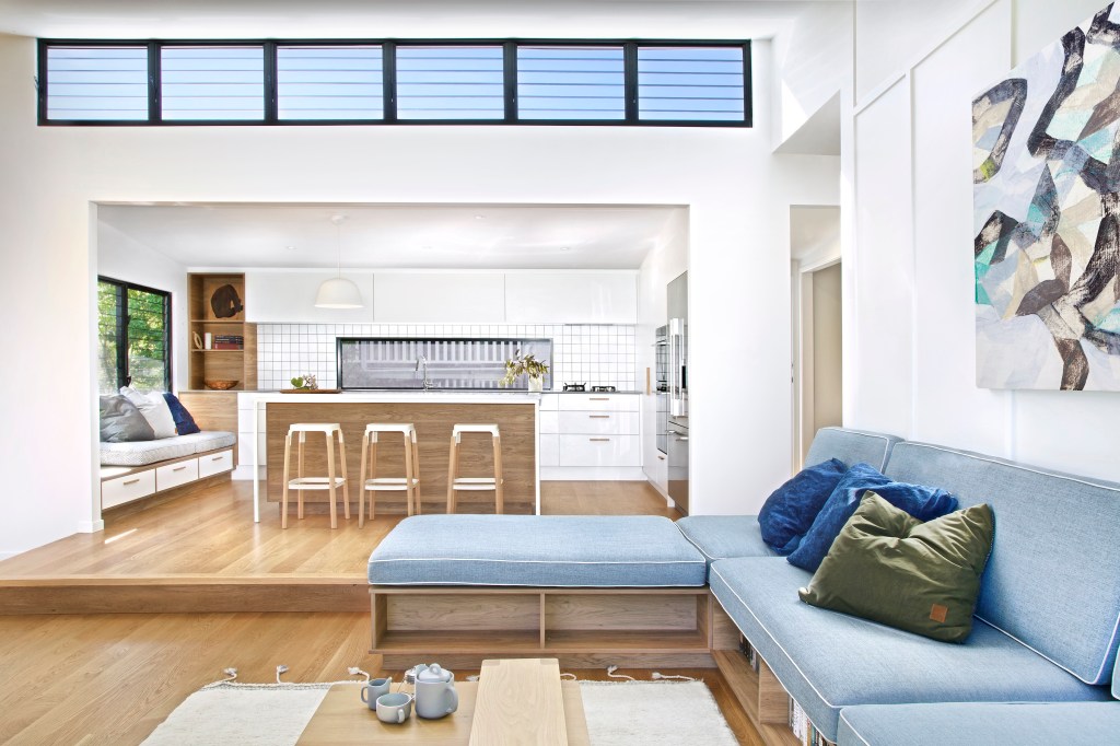 Sala de estar integrada com a cozinha, sofá com almofadas coloridas e base branca com madeira