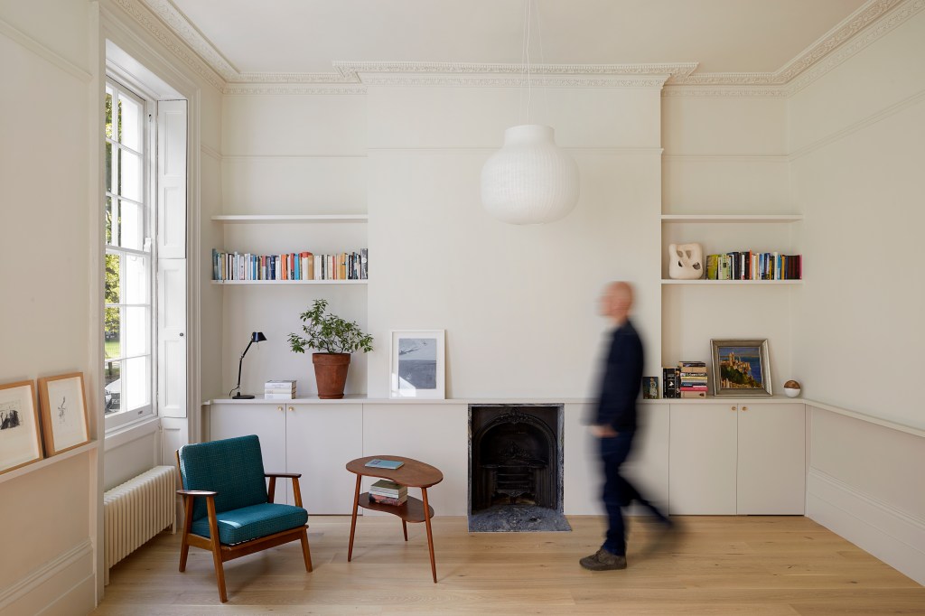 Sala com decoração neutra, piso de madeira, poltrona verde, prateleiras com livros, lareira