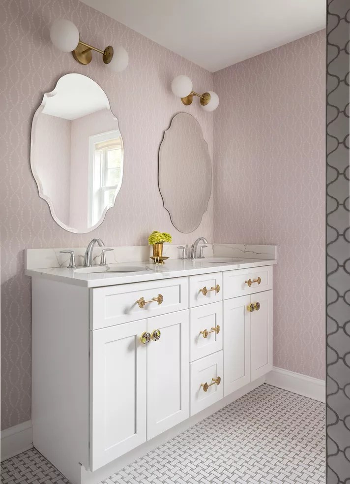 12 ideias fofas para decorar o banheiro-Victoria Bell Banheiro com paredes em rosa claro, armário de pia branco e puxadores e registros de água dourados.
