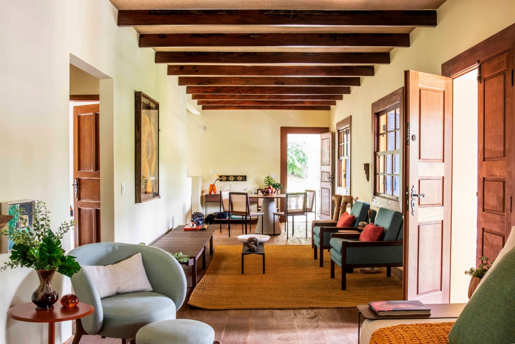 19-retrofit-em-duas-casas-de-familia-recupera-estilo-colonial-das-construcoes Sala de estar com poltrona cinza, sofá verde, vigas de madeira