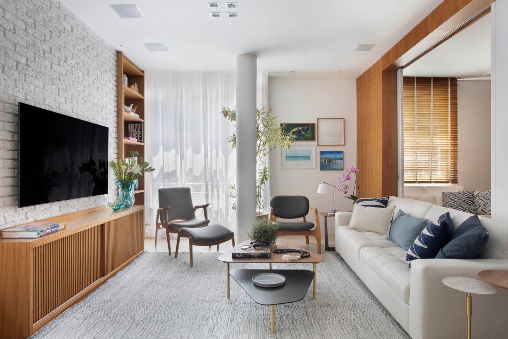 Sala de estar com sofá branco, painel de madeira e poltrona cinza