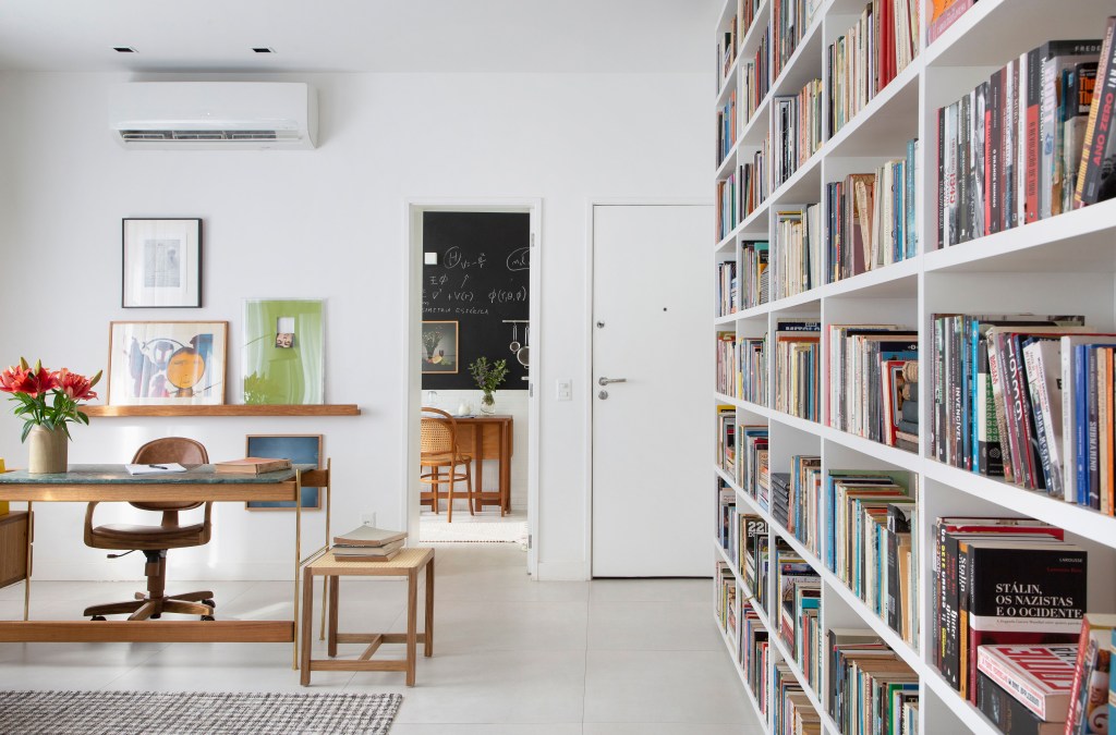 Sala de estar com décor claro, base branca e estante com muitos livros