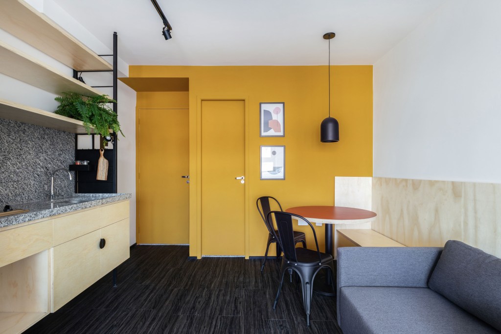 Estúdio com piso preto, parede amarela, luminária pendente e cadeiras pretas