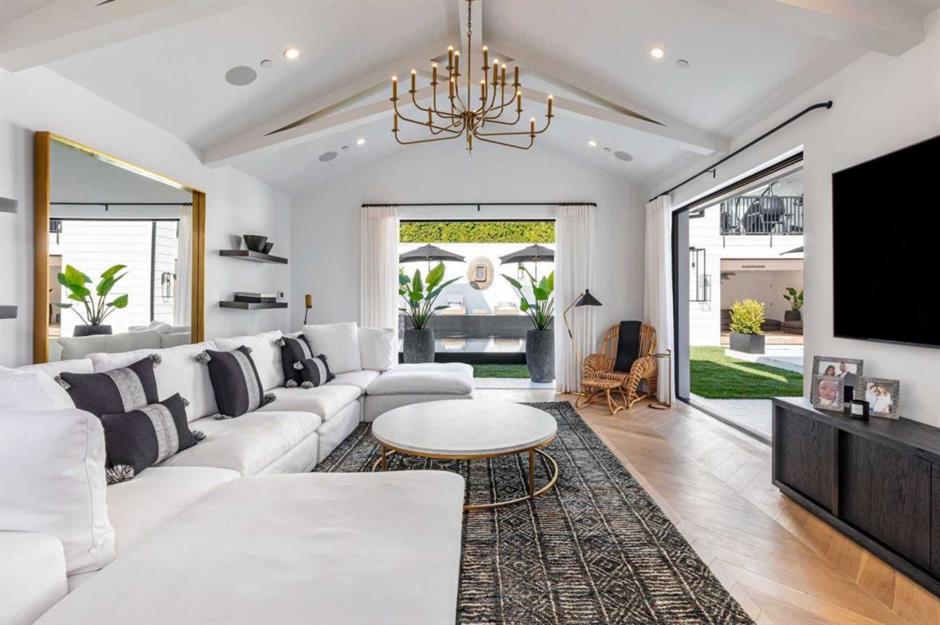 Sala da mansão de Rihanna em Beverly Hills com sofá branco em L, mesa de centro redonda, lustre, tapete e piso de madeira