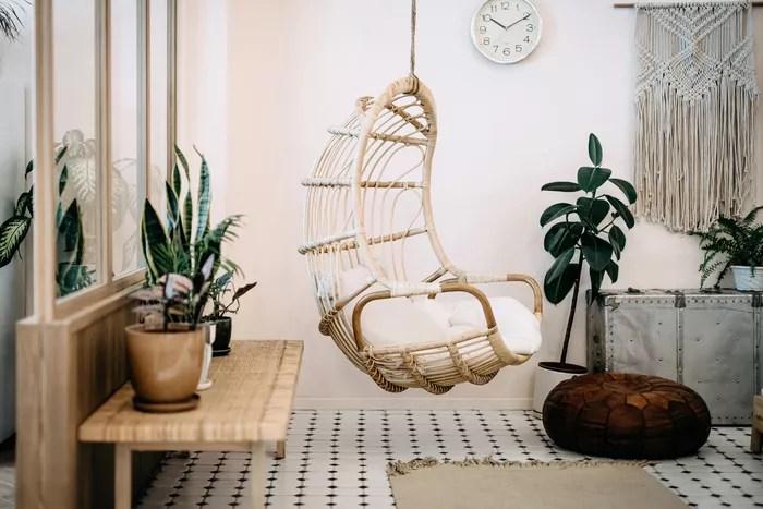 Cadeira de vime de balanço dentro de uma sala. Ambiente em tons de bege e branco, decorado por tapetes e plantas.