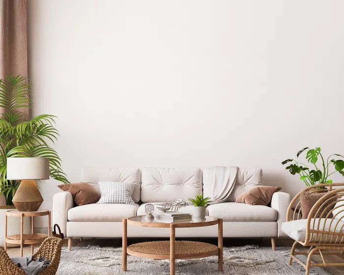 Sala de estar em tons de bege e branco, decorada por móveis de madeira, sofá cinza claro e plantas.