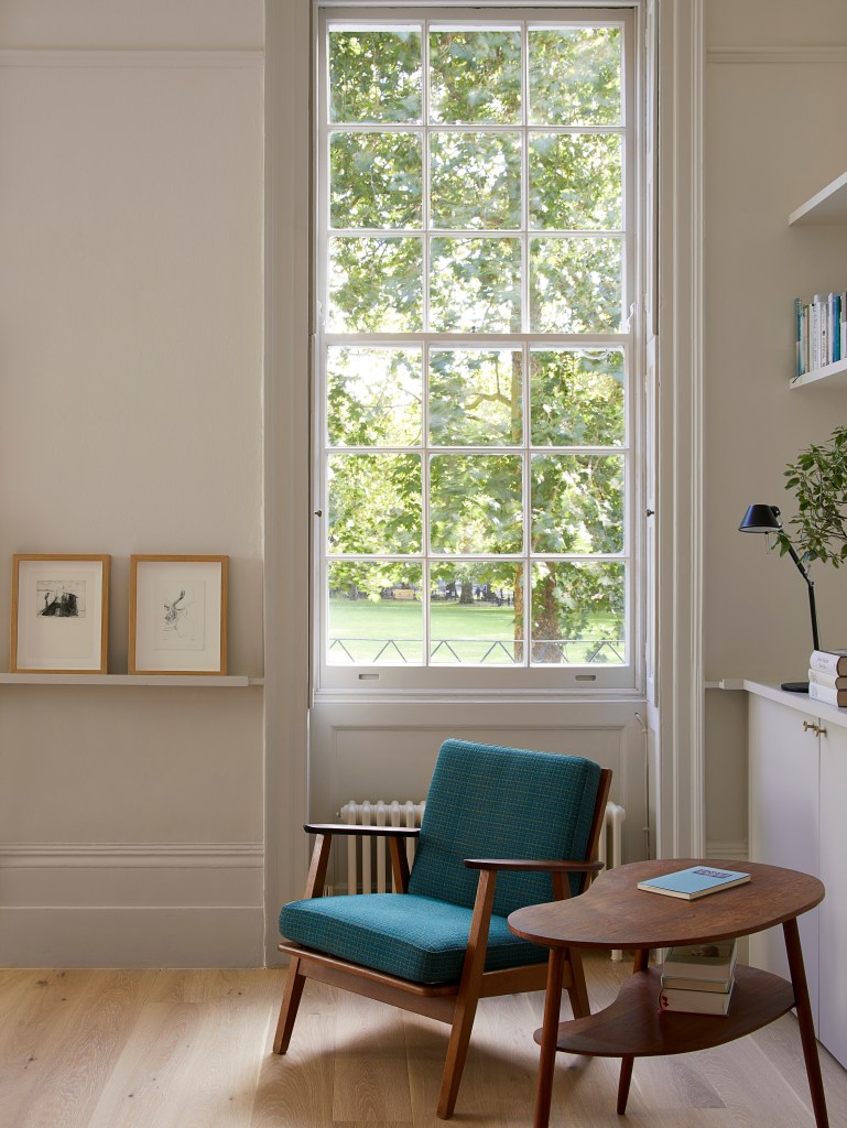 Detalhe de sala de estar com janela de vidro, poltrona verde e mesa de centro de madeira