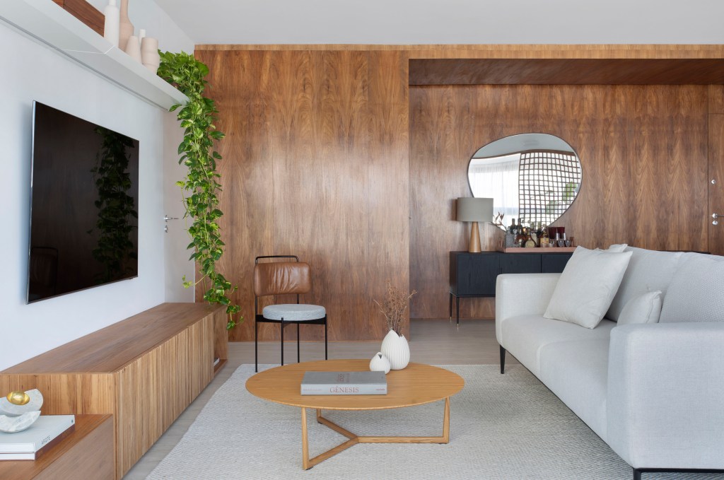 Sala de estar com painel de madeira, sofá branco e mesa de centro