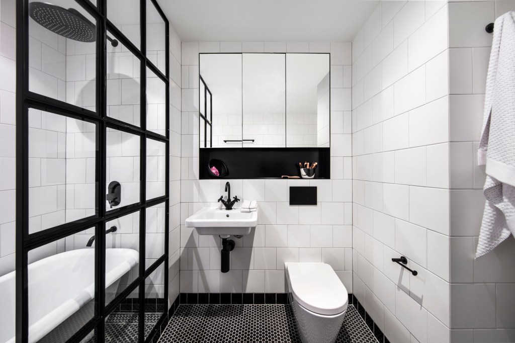 Banheiro com azulejos brancos e detalhes pretos, box de vidro
