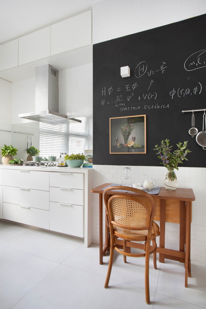 Cozinha com base branca, cadeira e mesa de madeira e parede com quadro negro