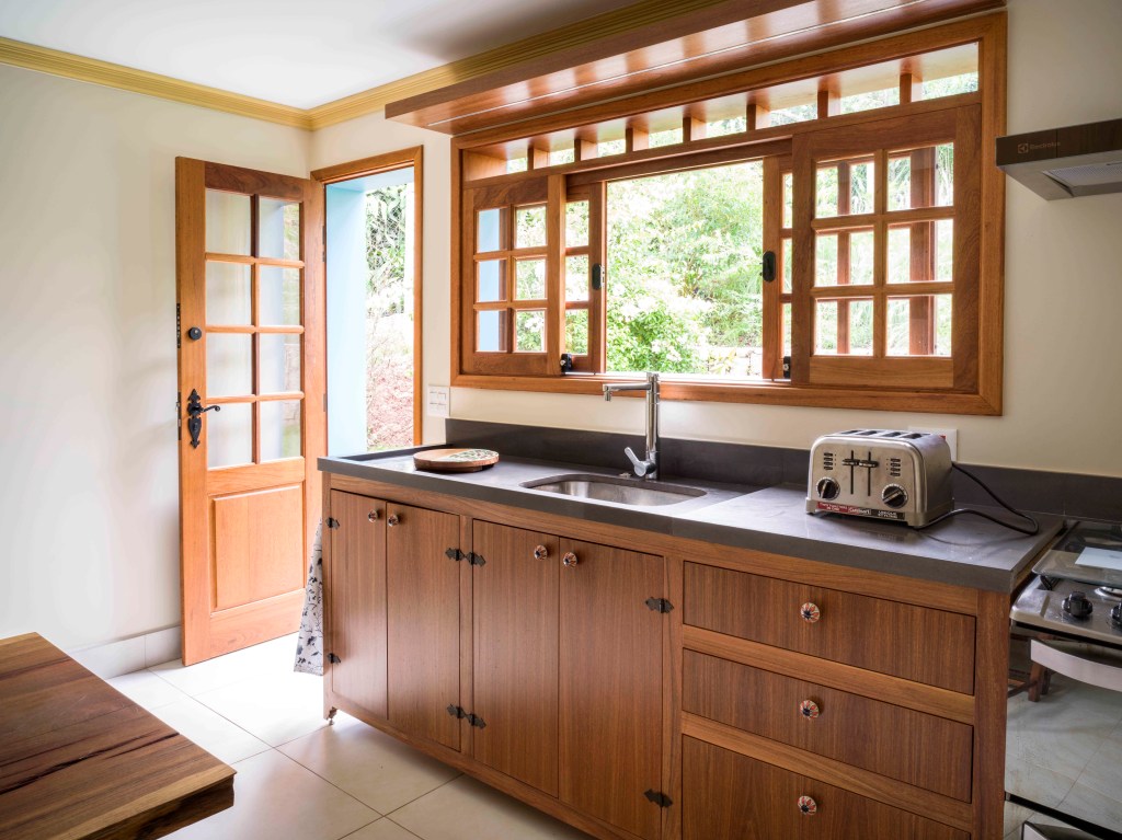 8-retrofit-em-duas-casas-de-familia-recupera-estilo-colonial-das-construcoes Cozinha com vista para a natureza e armários todos de madeira