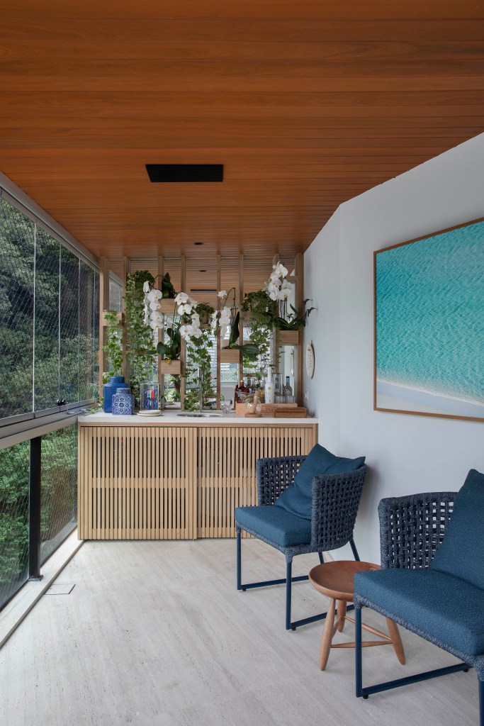 Varanda com cadeiras azuis, armário de madeira e vista para natureza