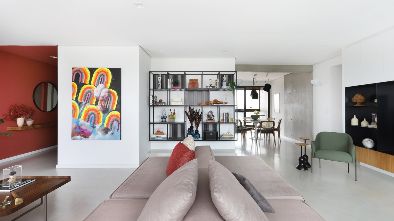 Sala de estar com sofá bege/cinza no meio, obra de arte colorida e estante modular ao fundo