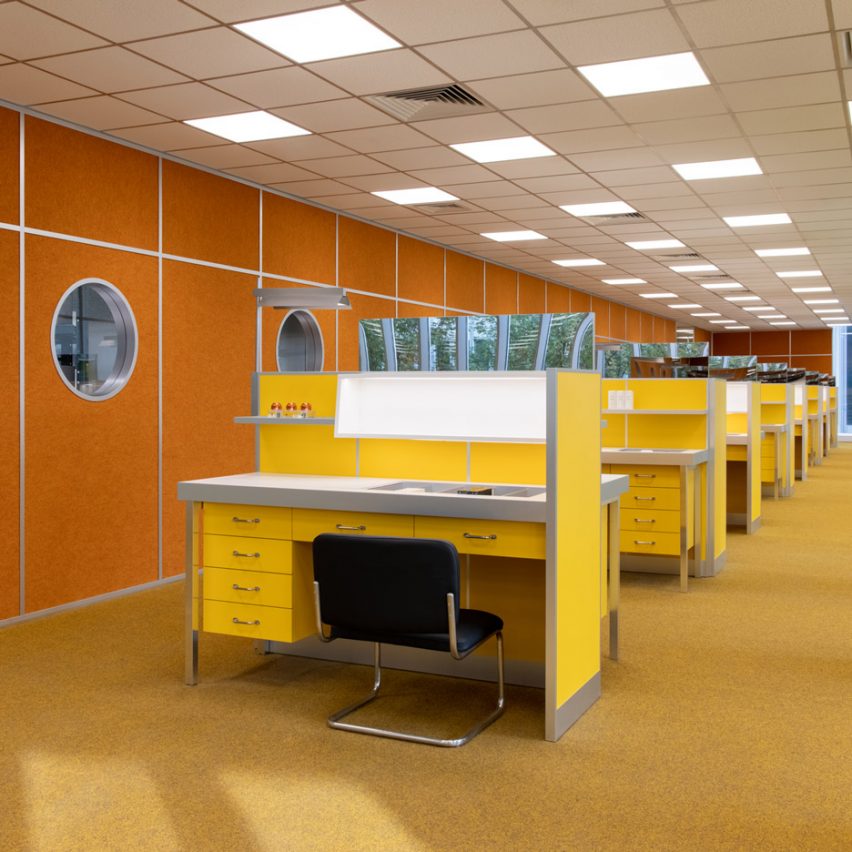 Loja de maquiagem com bancadas que parecem mesas de um escritório dos anos 70. Cores predominantes em tons amarelos e laranjas.